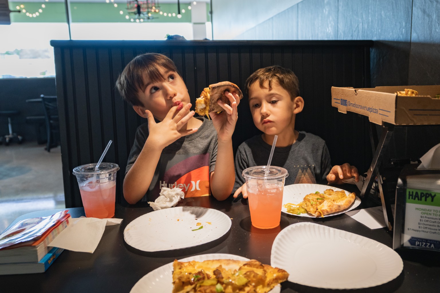 Two boys enjoying pizza in a booth at Madison Avenue Pizza